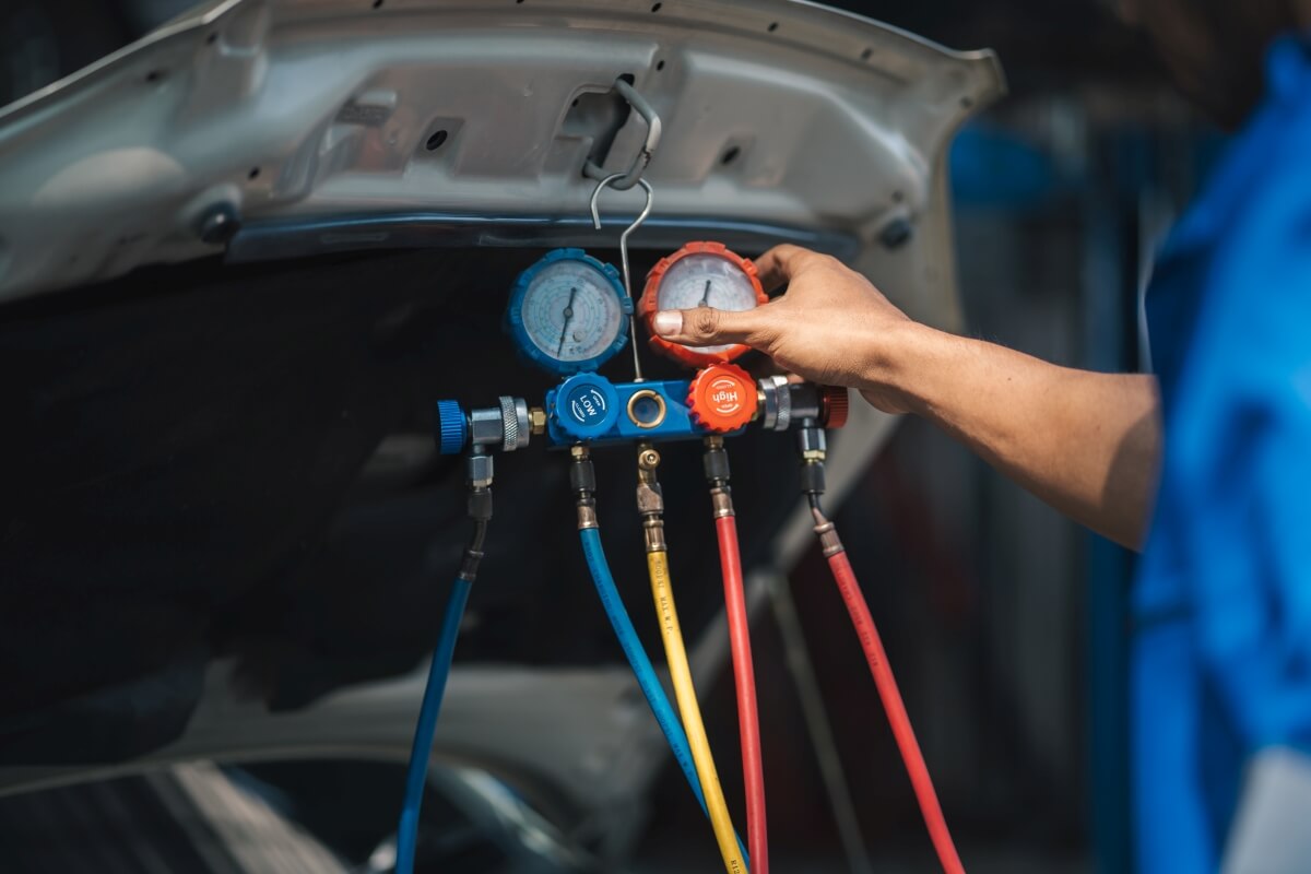 Ręka mechanika podczas naprawy klimatyzacji samochodowej z wykorzystaniem manometrów.