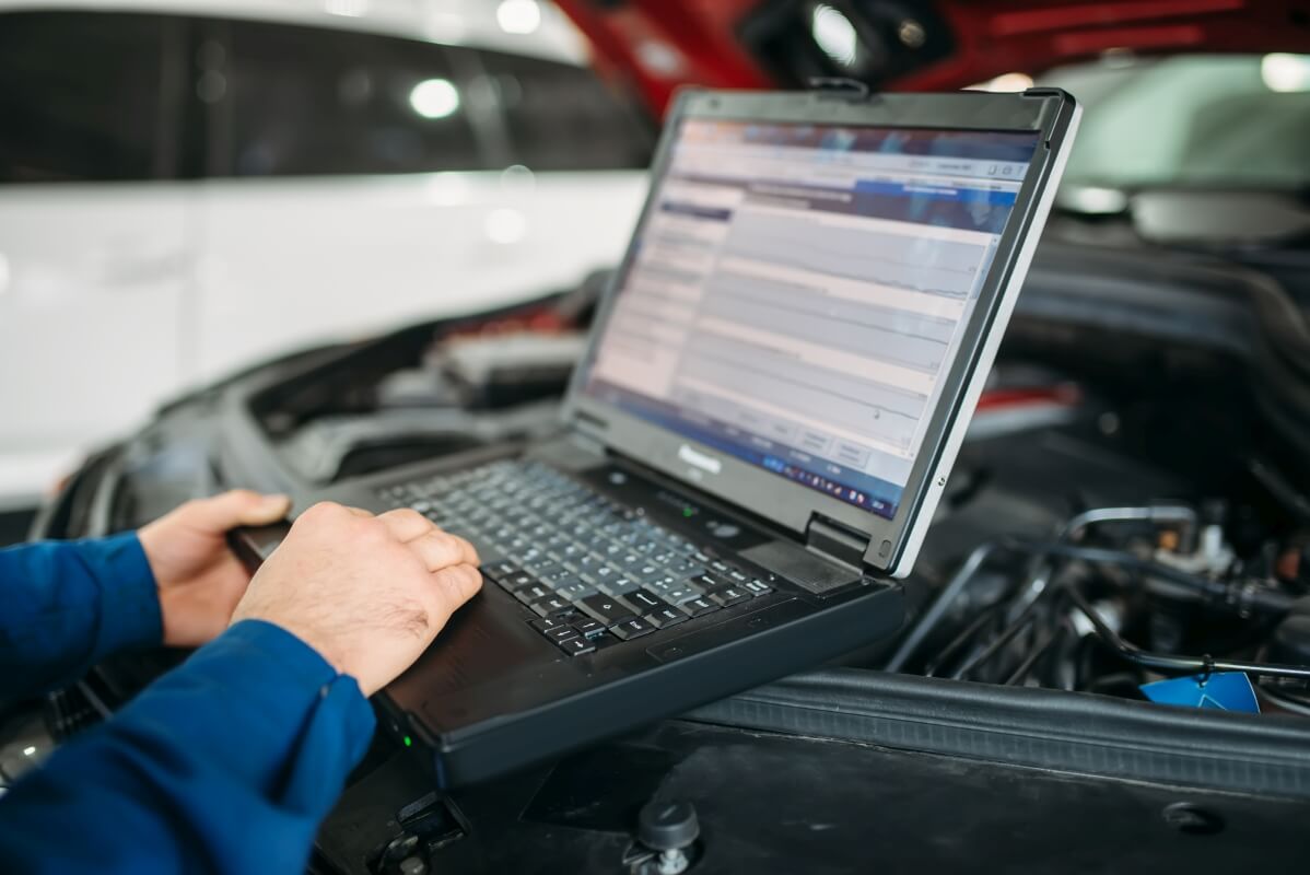 Mechanik przeprowadza diagnostykę komputerową silnika przy użyciu laptopa.