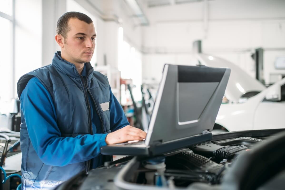 Mechanik przeprowadza diagnostykę komputerową silnika za pomocą laptopa.