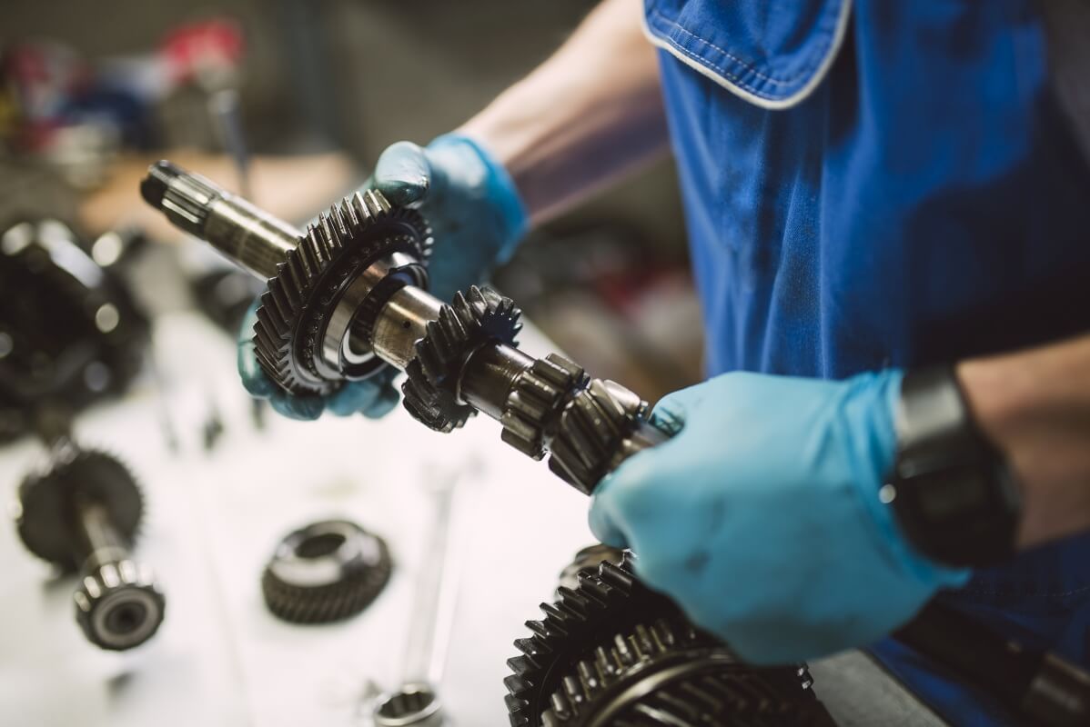Mechanik w rękawiczkach przeprowadza naprawę skrzyni biegów.