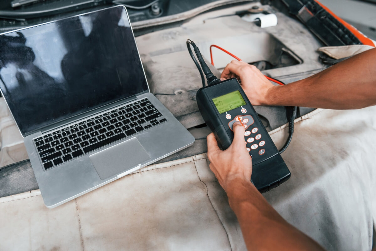 Osoba używa urządzenia diagnostycznego i laptopa do diagnostyki silników.
