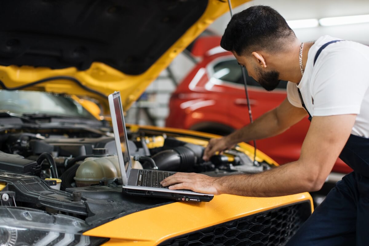 Mechanik przeprowadza diagnostykę komputerową silników, używając laptopa przy otwartej masce samochodu.